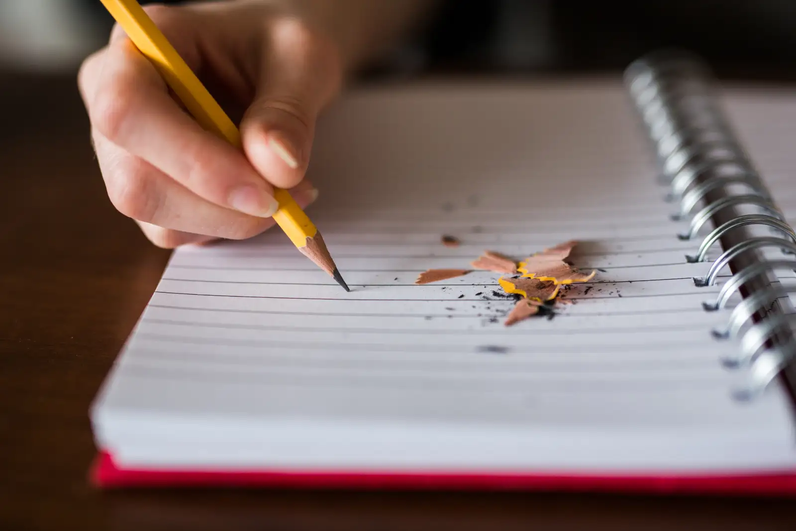 A hand holding a yellow pencil writing in a spiral-bound notebook